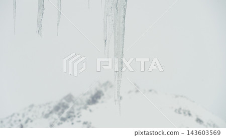 Long transparent icicles hanging over blurred snow-covered mountain ridge in winter Long transparent icicles hanging over blurred snow-covered mountain ridge in winter 143603569