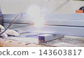 Close up of gloved worker welding metal beams with intense sparks and smoke during outdoor repair work, showing industrial fabrication, construction maintenance, steel surfaces, and bright sunlight 143603817
