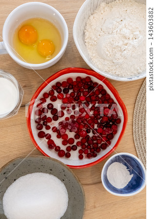 Baking ingredients. Cranberry recipe. Red berries raw eggs white flour sugar measured in ceramic bowls on wooden table background. Baking ingredients. Cranberry recipe. Red berries raw eggs white flour sugar measured in ceramic bowls on wooden table background. 143603882