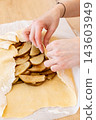 Fruit pastry. Cooking galette. Female baker hand covering sliced pear with flattered dough flour sheet on home kitchen paper parchment. 143603949