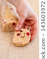 Pastry preparation. Homemade recipe. Female chef hand holding biscotti roll log dough piece with red berry on kitchen baking sheet. 143603972