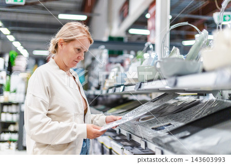 Woman Examining Merchandise in a Home Improvement Store Woman Examining Merchandise in a Home Improvement Store 143603993