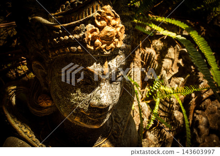 Balinese stone statue of Dewi Sri, the goddess of rice and prosperity, offering spiritual symbolism and cultural heritage in a lush tropical garden environment in Bali, Indonesia 143603997