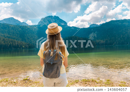 Woman with Backpack Facing Durmitor Mountains Across Black Lake Woman with Backpack Facing Durmitor Mountains Across Black Lake 143604057
