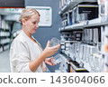 Woman Examining Glassware on a Retail Store Shelf 143604066