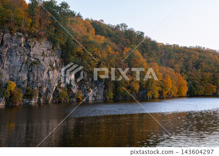 Autumn Forest Reflected Across Quiet Lake. Peaceful autumn nature concept symbolizing seasonal transformation harmony and beauty of untouched landscapes Autumn Forest Reflected Across Quiet Lake. Peaceful autumn nature concept symbolizing seasonal transformation harmony and beauty of untouched landscapes 143604297