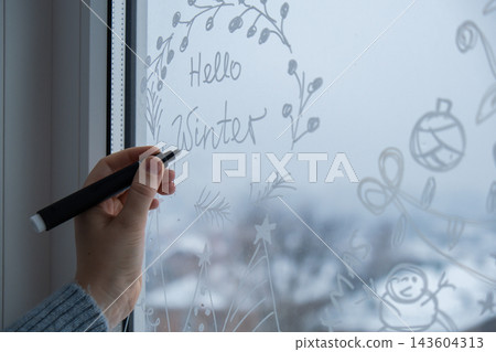 Sustainable responsible holiday decor. Hello winter text painted on window glass indoor at home. Christmas winter decoration. White pattern. Snow art tracery on season. Diy Sustainable responsible holiday decor. Hello winter text painted on window glass indoor at home. Christmas winter decoration. White pattern. Snow art tracery on season. Diy 143604313