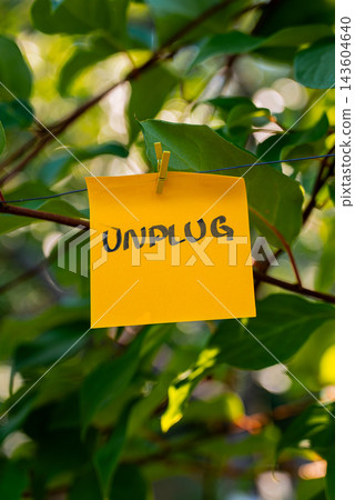 Paper note with UNPLUG message against green leafy background. Suitable for digital detox, screen-free lifestyle technology break mindfulness. Paper note with UNPLUG message against green leafy background. Suitable for digital detox, screen-free lifestyle technology break mindfulness. 143604640