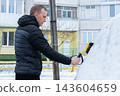 Man Brushing Snow Off Car During Winter. Seasonal outdoor activity shows vehicle maintenance snow removal and preparation for driving in cold conditions 143604659