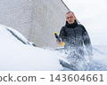 Man Brushing Snow Off Car During Winter. Seasonal outdoor activity shows vehicle maintenance snow removal and preparation for driving in cold conditions 143604661