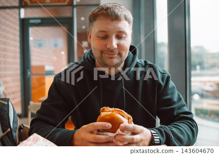 Hungry man holding a big juicy burger in a fast food cafe Hungry man holding a big juicy burger in a fast food cafe 143604670