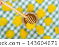 Top view flat lay Transparent glass of jar dandelion jelly wooden honey dipper coated with jelly dripping with dandelion flowers in vase. Soft natural lighting highlights the amber color glossy 143604671