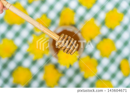 Top view flat lay Transparent glass of jar dandelion jelly wooden honey dipper coated with jelly dripping with dandelion flowers in vase. Soft natural lighting highlights the amber color glossy Top view flat lay Transparent glass of jar dandelion jelly wooden honey dipper coated with jelly dripping with dandelion flowers in vase. Soft natural lighting highlights the amber color glossy 143604671