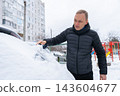 Driver Clears Snow From Windshield Before Winter Journey. Everyday cold-weather routine highlights seasonal vehicle care practical winter preparation outdoor maintenance and safe travel during snowy c 143604677