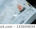 Driver Watches Man Clear Snow From Windshield During Winter. View from inside car shows man outside removing accumulated snow from windshield with handheld brush.  143604694