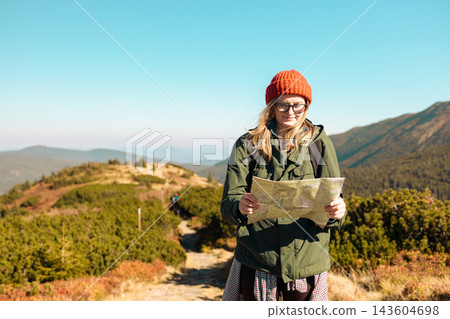 Young woman hiker with paper map planning route in mountains Young woman hiker with paper map planning route in mountains 143604698