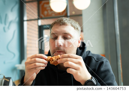 Hungry man eating crispy fried chicken in a fast food restaurant Hungry man eating crispy fried chicken in a fast food restaurant 143604753