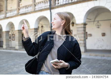 Smiling young woman pointing finger away in European city 143604754