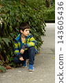 Thoughtful little boy sitting near green plants in park 143605436