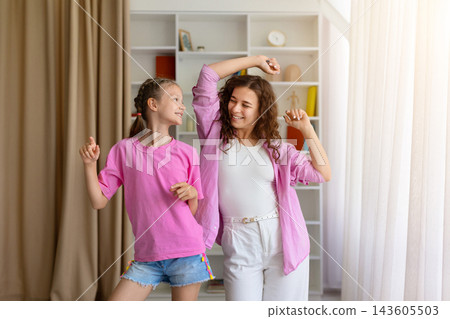 Cheerful mother and young daughter are dancing together at home Cheerful mother and young daughter are dancing together at home 143605503