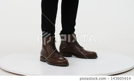 Person wearing brown leather lace-up boots and black trousers, showcasing male footwear fashion on a white background 143605914