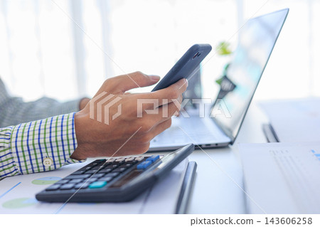 Businessman working in office using smartphone and typing on laptop with graph data and calculator at desk. Businessman working in office using smartphone and typing on laptop with graph data and calculator at desk. 143606258