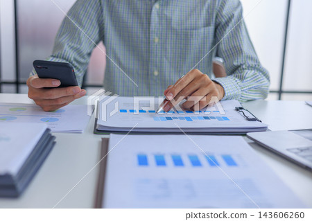 Professional financial analyst working on analyzing charts and documents using smartphone in modern office. Professional financial analyst working on analyzing charts and documents using smartphone in modern office. 143606260