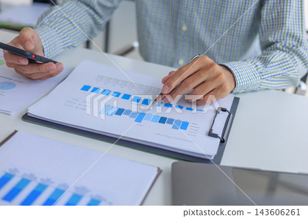 Businessman working in office using smartphone while reviewing and analyzing graph data at desk. Businessman working in office using smartphone while reviewing and analyzing graph data at desk. 143606261