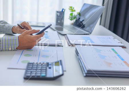 Professional financial analyst working on analyzing charts and documents using smartphone in modern office. Professional financial analyst working on analyzing charts and documents using smartphone in modern office. 143606262