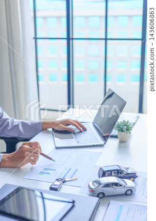 Businessman using laptop and analyzing financial documents for car purchase agreement in office Businessman using laptop and analyzing financial documents for car purchase agreement in office 143606863