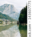 Wooden boathouse on calm lake reflecting alpine mountains and village 143607775