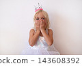 Blonde Girl Wearing Princess Crown and Dress Covering Mouth with Hands  143608392