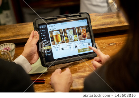 顧客在居酒屋(日本酒吧)櫃檯用平板電腦點餐時的雙手。 顧客在居酒屋(日本酒吧)櫃檯用平板電腦點餐時的雙手。 143608816