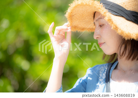 A profile view of a female model shielding herself from the sun with a straw hat. A profile view of a female model shielding herself from the sun with a straw hat. 143608819