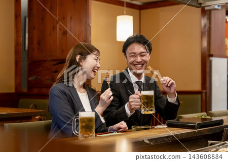 A man and a woman enjoying yakitori and beer at the counter seats. A man and a woman enjoying yakitori and beer at the counter seats. 143608884