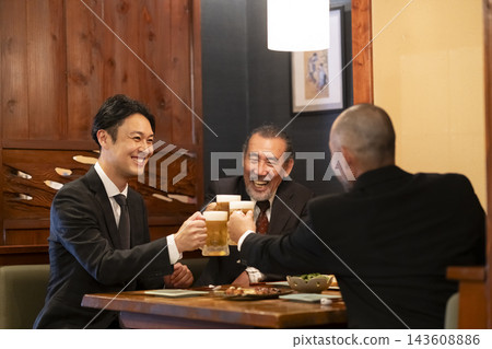 A group of businessmen toasting with draft beer at an izakaya (Japanese pub). A group of businessmen toasting with draft beer at an izakaya (Japanese pub). 143608886