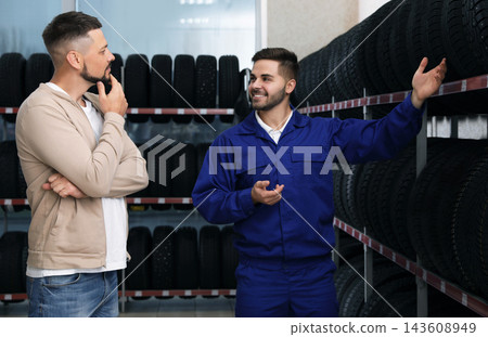 Mechanic helping client to choose car tire in auto store Mechanic helping client to choose car tire in auto store 143608949