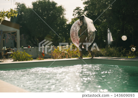 Bride holding a transparent pool ring beside a garden swimming pool 143609093