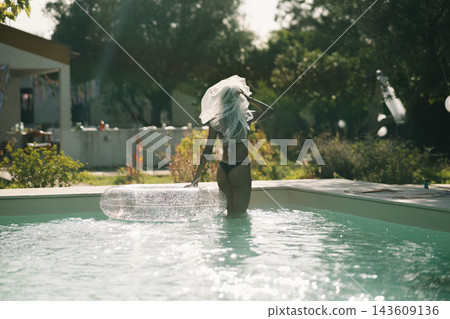 Bride in a black bikini and white veil standing in the swimming pool 143609136