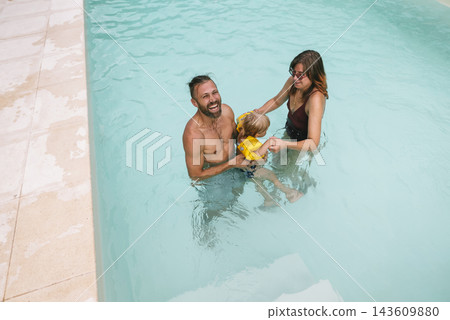 Adults Hold Child Steady In Turquoise Pool Adults Hold Child Steady In Turquoise Pool 143609880