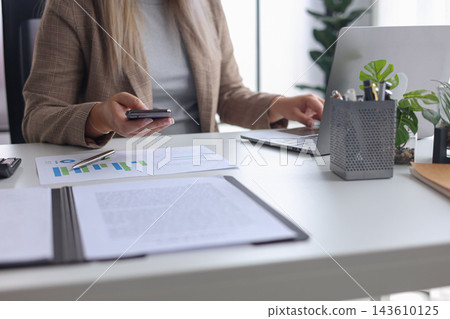 Female Professional Reviewing Statistical Reports with Laptop and Smartphone. Female Professional Reviewing Statistical Reports with Laptop and Smartphone. 143610125