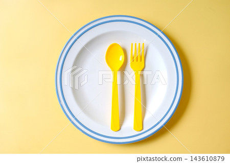 Yellow spoon and fork on white plate over color background. Yellow spoon and fork on white plate over color background. 143610879