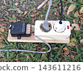 Outdoor electrical extension cord with black sensor module and white sockets. Temporary power solution for garden lighting or event equipment. 143611216