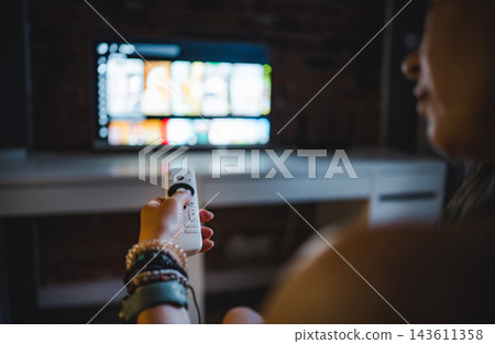 Young Woman In A Dark Room Watching A Smart Tv And Changing Channels With A Remote Young Woman In A Dark Room Watching A Smart Tv And Changing Channels With A Remote 143611358