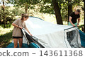 Father and daughter are pitching a tent in a wooded area during daytime 143611368