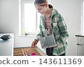 Girl stands in kitchen organizing utensils while holding a basket 143611369