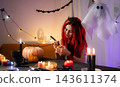 Cute Little Girl In A Halloween Witch Wig Plays With A Pumpkin, Drawing A Spooky Face 143611374