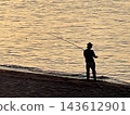 The silhouette of a fisherman fishing on the beach, shimmering in the setting sun. 143612901