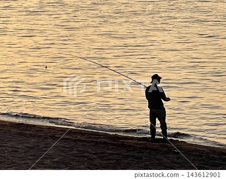 The silhouette of a fisherman fishing on the beach, shimmering in the setting sun. The silhouette of a fisherman fishing on the beach, shimmering in the setting sun. 143612901