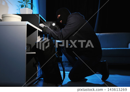 Thief taking money out of steel safe indoors at night Thief taking money out of steel safe indoors at night 143613269